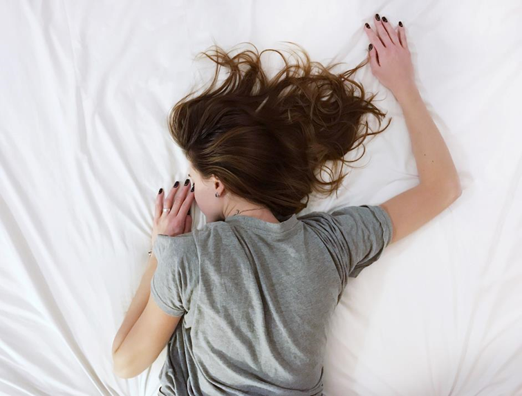 Image of a woman wearing a grey top lying face down on a bed