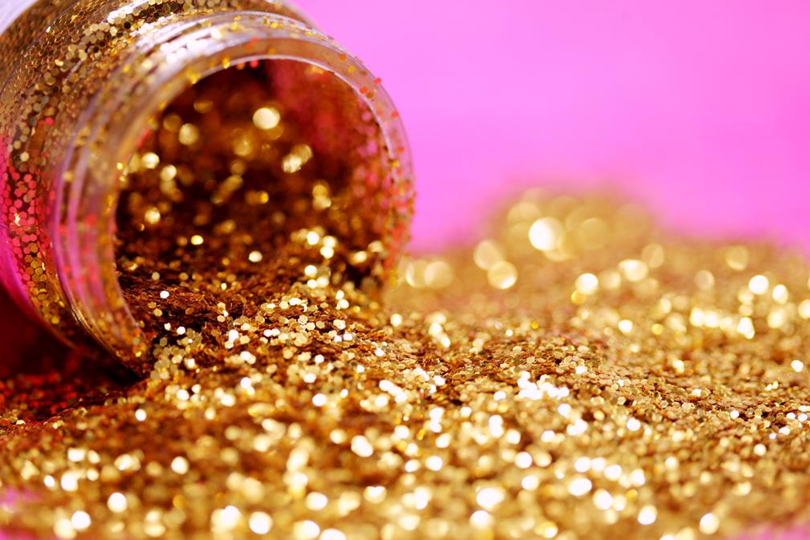 Image of gold glitter spilling out of a jar against a pink background